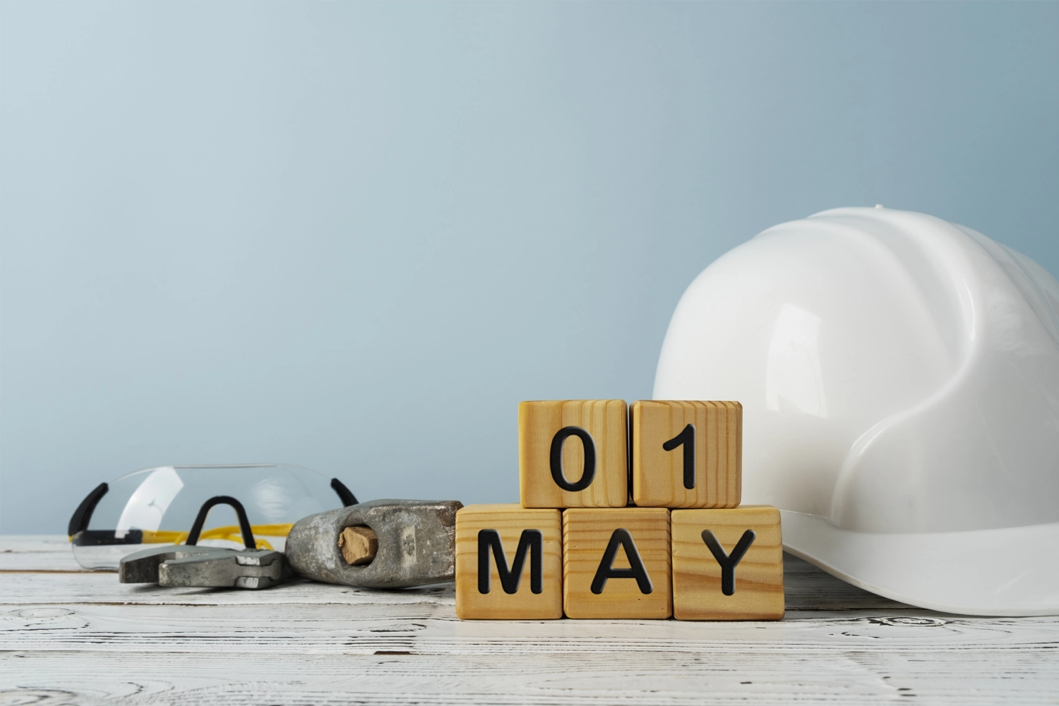Elmetto di protezione, occhiali di sicurezza e blocchi in legno con la data 01 May per la pianificazione dei corsi di sicurezza sul lavoro.
